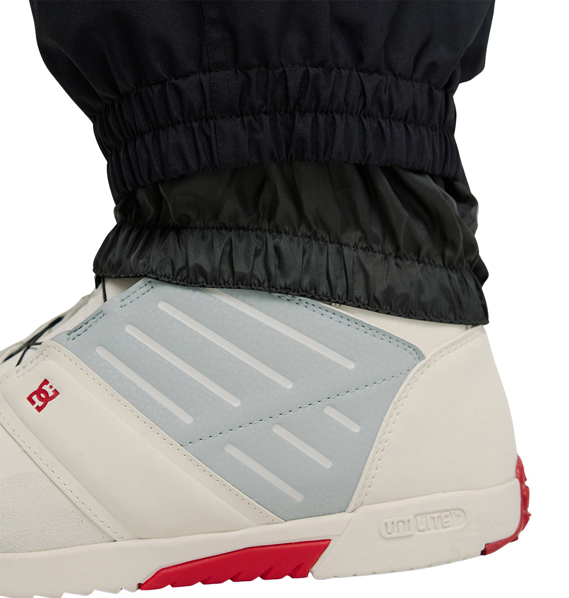 A close-up of a person’s lower leg wearing DC Shoes’ Smoke Pants 10K tucked into a light gray and white sneaker with red accents and the word UNILITE embossed on the sole, showcasing breathable protection for all-day comfort.