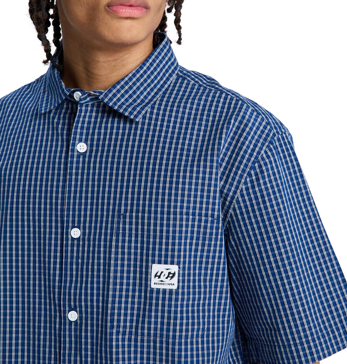 A person wearing the Reebok Game On Ss blue and white checkered short-sleeve button-up shirt with a white chest pocket label. Their face is partially visible.