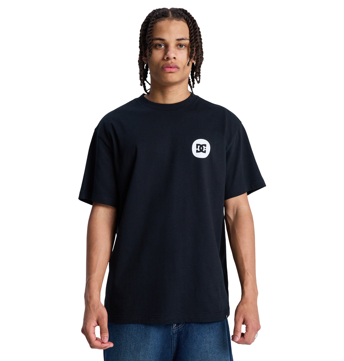 A person with braided hair wears a loose black Reebok Shape Or Destroy Hss t-shirt with a small white logo on the left chest and blue jeans, standing against a white background.