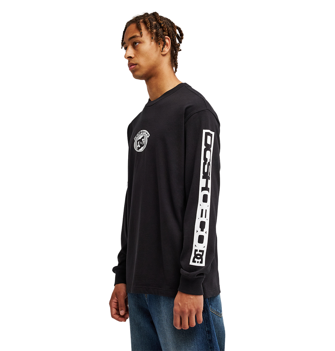 A young man stands sideways against a plain white background, wearing blue jeans and the Men's DC Echo Tee by DC Shoes—a black graphic t-shirt featuring DC artwork on the chest and sleeve.