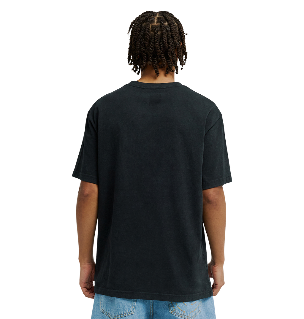 A person with short, twisted braids is shown from behind, wearing a relaxed fit black Men's DC Star Struck Tee by DC Shoes and light blue denim shorts against a plain white background.