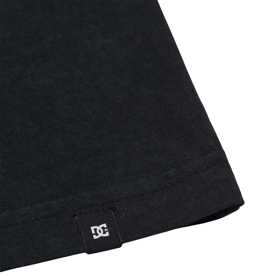 Close-up of the bottom hem of the Men's DC Star Struck Tee by DC Shoes, featuring a small black fabric tag with the white DC Shoes logo sewn into the hem.