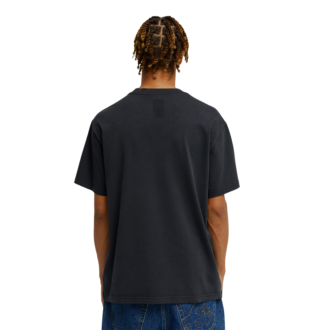 A person with braided hair is seen from behind, wearing the Men's DC Speratic Tee by DC Shoes in black paired with blue jeans against a plain white background.