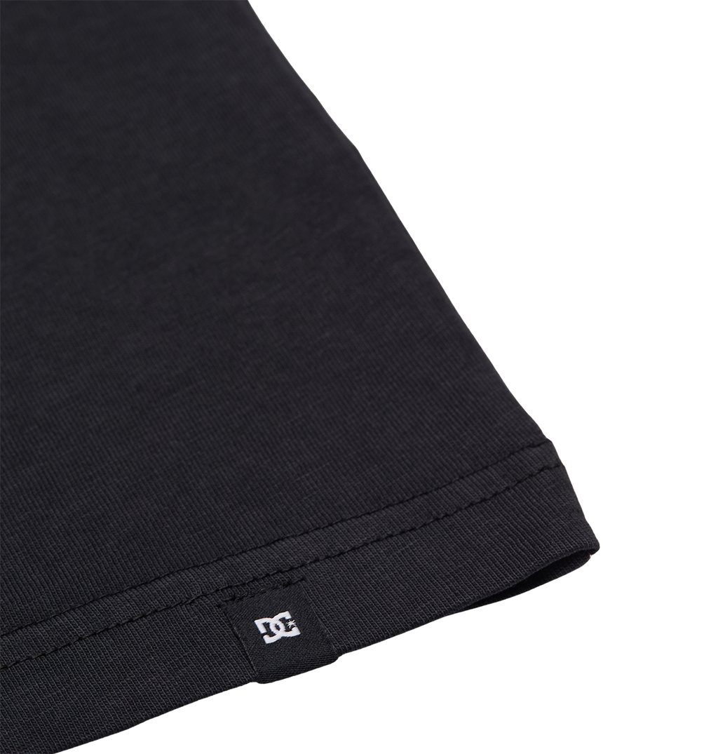 Close-up of the hem of the Men's DC Speratic Tee by DC Shoes in black, highlighting detailed stitching and a small white DC logo tag sewn into the bottom edge, set against a plain white background.